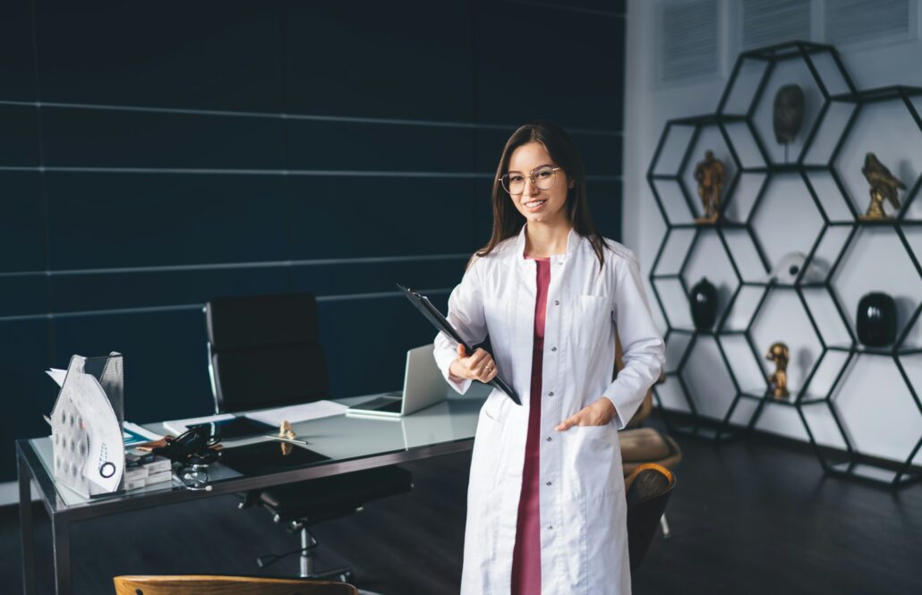 Smiling female doctor standing in office with hand in pocket