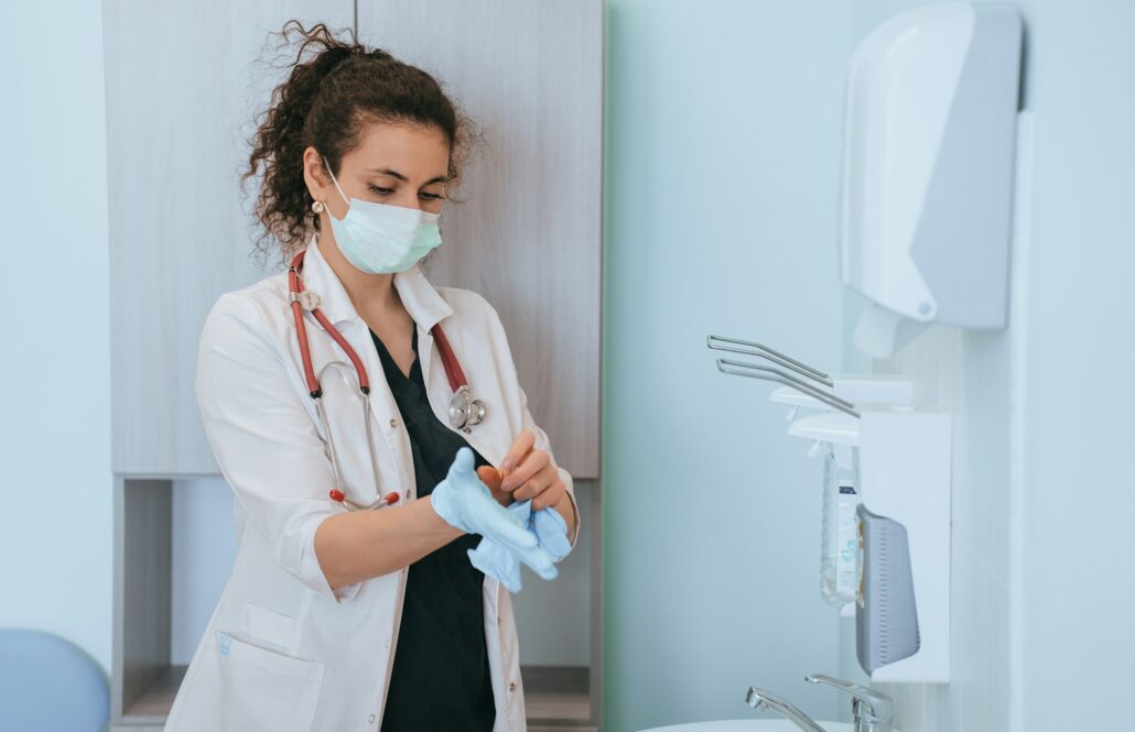 female doctor in protective face mask at medical office putting on rubber gloves preparing for exam