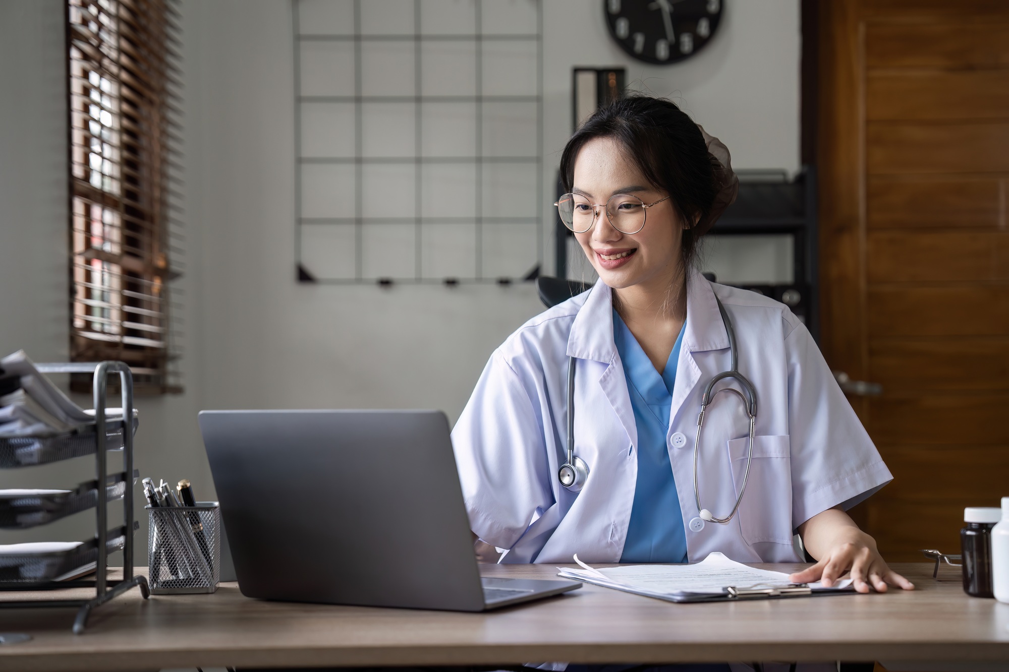 Beautiful female doctor checking patient information working with laptop on desk in doctor's office